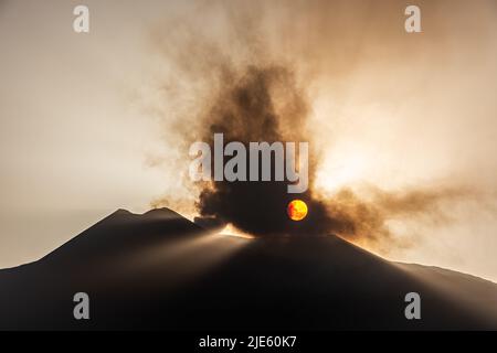 Die untergehende Sonne, die durch eine Wolke vulkanischer Asche vom Ätna auf Sizilien, dem aktivsten Vulkan Europas, ausbricht Stockfoto