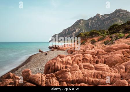 Der graue Kiesstrand Coccorocci, eingerahmt von roten Porphyrfelsen, und die Wälder rund um den Monte Cartucceddu an der Ostküste Sardiniens, Ogliastra, Italien Stockfoto