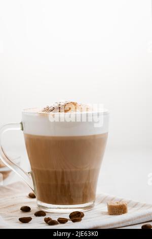 Latte-Kaffee, der in Schichten mit Schaum und einer knusprigen Schokoladenplatte auf einem hellen Küchentisch gegossen wird. Vertikales Bild mit Kopierbereich. Stockfoto