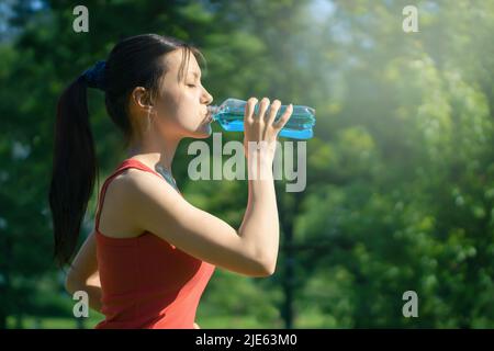 Schöne junge Frau joggt morgens im Park und trinkt blaue Isotone aus einer Flasche. Stockfoto