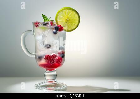 Erfrischender Sommercocktail mit Eis, Limette und Beeren in einem Glas, Copyspace. Stockfoto