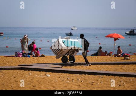 (220625) -- GOZO, 25. Juni 2022 (Xinhua) -- Ein Mitarbeiter trägt Strandliegen in einem Trolley am Ramla-Strand auf der Insel Gozo, Malta, 25. Juni 2022. (Foto von Jonathan Borg/Xinhua) Stockfoto