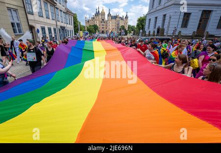 Schwerin, Deutschland. 25.. Juni 2022. Mit einer großen Regenbogenflagge marschieren die Teilnehmer beim Christopher Street Day 16. vom Schloss in die Innenstadt unter dem Motto „Wissen schafft Vielfalt“. Bunt kostümiert treffen sich die meist jüngeren Menschen im Alten Garten. Die CSD soll die Menschen an die Rechte von Lesben, Schwulen, Bisexuellen, Transgender, Intersex und queeren Menschen erinnern. Quelle: Jens Büttner/dpa/Alamy Live News Stockfoto