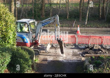Arbeiter, der einen Minibagger benutzt, um einen Bürgersteig an einer Straße in einem Wohngebiet zu graben Stockfoto
