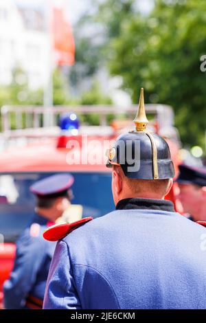 Hannover, Deutschland. 25.. Juni 2022. Eine Person mit historischer Feuerwehruniform steht am Trammplatz in der Innenstadt von Hannover zum Tag der deutschen Feuerwehrleute 29. vor einem Feuerwehrauto. Kredit: Michael Matthey/dpa/Alamy Live Nachrichten Stockfoto