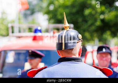 Hannover, Deutschland. 25.. Juni 2022. Eine Person mit historischer Feuerwehruniform steht am Trammplatz in der Innenstadt von Hannover zum Tag der deutschen Feuerwehrleute 29. vor einem Feuerwehrauto. Kredit: Michael Matthey/dpa/Alamy Live Nachrichten Stockfoto