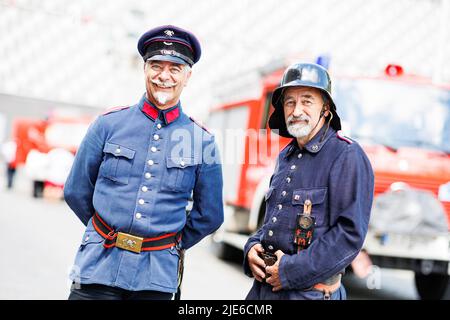 Hannover, Deutschland. 25.. Juni 2022. Die Brüder Dirk Niedzella (l.) und Uwe Niedzella stehen beim Deutschen Feuerwehrtag 29. auf dem Trammplatz in der Innenstadt Hannovers in historischen Feuerwehruniformen vor Feuerwehrfahrzeugen. Kredit: Michael Matthey/dpa/Alamy Live Nachrichten Stockfoto