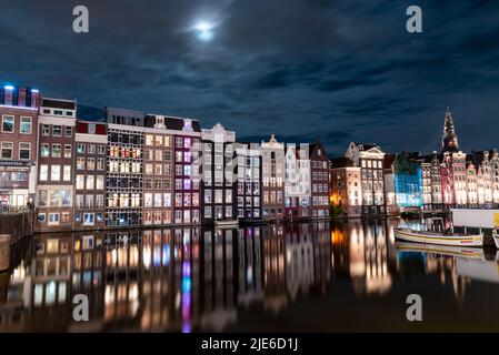 Nachtblick auf Amsterdam mit beleuchteten Kanalhäusern und Reflexionen auf dem Wasser. Das Bild fängt die historische Architektur und das friedliche A der Stadt ein Stockfoto