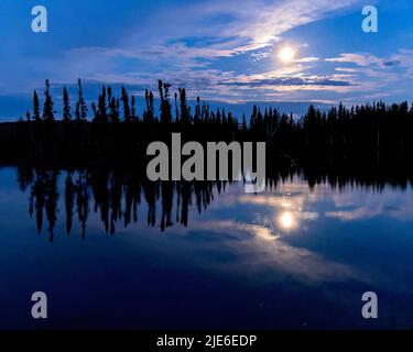 Ein nördlicher Saskatchewan-Vollmond spiegelt sich in den Gewässern eines Sees wider. Stockfoto