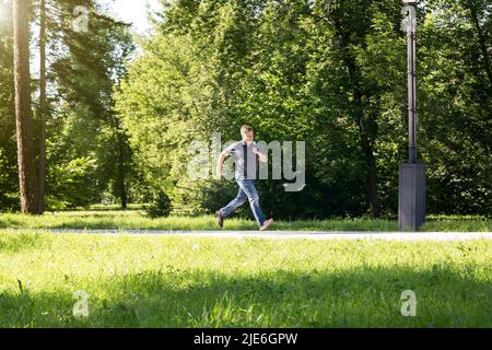 Ein männlicher blonder Verbrecher läuft vor dem Tatort im Stadtpark. Stockfoto