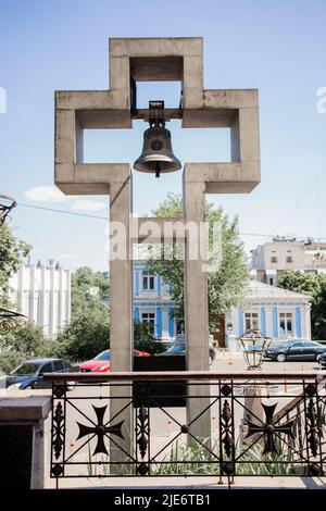 Ein Kreuz mit einer großen Glocke in der Nähe der katholischen Kirche Stockfoto