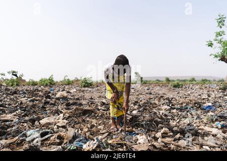 Das junge afrikanische Mädchen gräbt in einer Müllhalde auf der Suche nach wiederverwendbarem Material; informelles Abfallrecycling Stockfoto