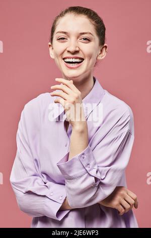Vertikales Porträt einer jungen Frau, die im Studio vor rosa Hintergrund lacht Stockfoto