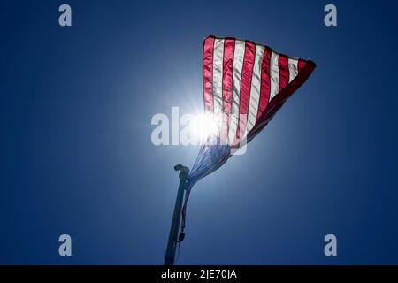 Ein Blick aus dem niedrigen Winkel auf eine amerikanische Flagge, die von der im Wind wehenden Sonne beleuchtet wird. Stockfoto