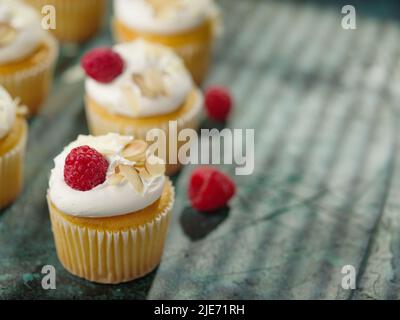 Appetitliche Muffins mit Rahm und Himbeeren auf dunkelgrünem Hintergrund. Auf dem Foto befinden sich keine Personen. Es gibt einen Platz zum Einfügen. Banner, bi Stockfoto