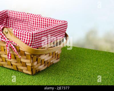 Stilvoller Picknickkorb aus Stroh auf hellgrünem Gras auf weißem Hintergrund. Sommerurlaub, Picknick. Minimalismus. Auf dem Foto befinden sich keine Personen. Dort Stockfoto