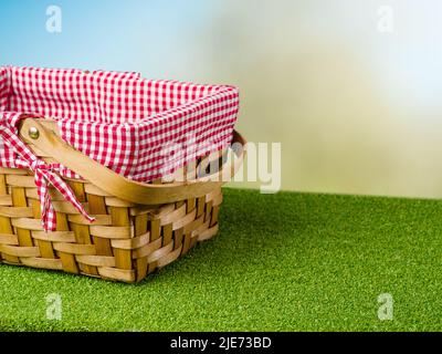 Auf dem grünen Gras ein Picknickkorb auf hellblauem Hintergrund. Familienurlaub, romantischer Spaziergang. Minimalismus. Auf dem Foto befinden sich keine Personen. Es ist ja so Stockfoto