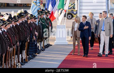 Elmau, Deutschland. 25.. Juni 2022. Frankreichs Staatspräsident Emmanuel Macron (m) und seine Frau Brigitte laufen am Münchner Flughafen vorbei, nachdem sie mit dem bayerischen Ministerpräsidenten Markus Söder (r, CSU) am Münchner Flughafen angekommen sind. Deutschland ist Gastgeber des Gipfels der wirtschaftlich starken Demokratien G7. Am ersten Tag des Gipfels werden die globale Wirtschaftslage, der Klimaschutz sowie die Außen- und Sicherheitspolitik mit den Sanktionen gegen Russland diskutiert. Quelle: Daniel Karmann/dpa/Alamy Live News Stockfoto