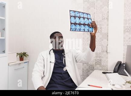 Ein afroamerikanischer Arzt untersucht die MRT-Bilder aufmerksam, während er im Büro sitzt Stockfoto