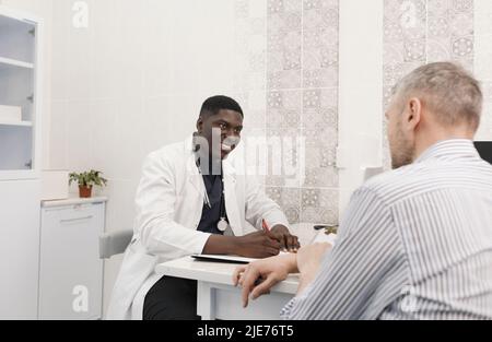 Ein junger afrikanischer Arzt konsultiert einen männlichen Patienten während eines Termins im Büro Stockfoto