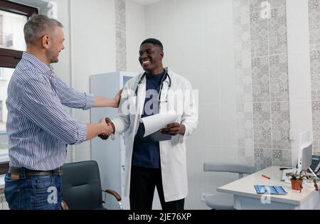 Lächelnder afroamerikanischer Arzt schüttelt einem zufriedenen Patienten die Hände Stockfoto