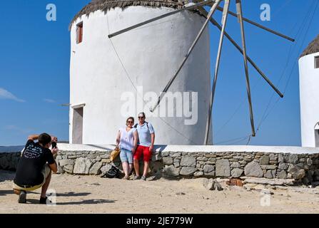 Mykonos, Griechenland - Juni 2022: Menschen, die für ein Foto vor einer der berühmten Windmühlen auf der griechischen Insel Mykonos posieren Stockfoto