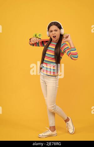 Unglücklicher Kinder-Skateboarder hört Musik in Kopfhörern mit Penny Board Skateboard, Hipster Stockfoto