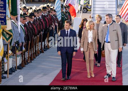 München, Deutschland. 25.. Juni 2022. Frankreichs Staatspräsident Emmanuel Macron (l.) und seine Frau Brigitte laufen am Münchner Flughafen vorbei an bayerischen Berggeflemen und Trachten, nachdem sie mit dem bayerischen Ministerpräsidenten Markus Söder (r., CSU) am Flughafen München angekommen sind. Deutschland ist Gastgeber des Gipfels der wirtschaftlich starken Demokratien G7. Am ersten Tag des Gipfels werden die globale Wirtschaftslage, der Klimaschutz sowie die Außen- und Sicherheitspolitik mit den Sanktionen gegen Russland diskutiert. Quelle: Daniel Karmann/dpa/Alamy Live News Stockfoto