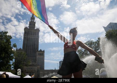 Warschau, Polen. 25.. Juni 2022. Eine Frau, die die Regenbogenfahne schwenkt, steht neben dem Brunnen und mit dem Palast der Kultur und Wissenschaft im Hintergrund, als sie an der Warschauer Gleichstellungsparade teilnimmt. Die Parade wurde organisiert, um die soziale Gleichheit zu fördern und die Aufmerksamkeit auf die Probleme der LGBT-Gemeinschaft in Polen zu lenken. In diesem Jahr fand auf der Warschauer Equality Parade die Kyiv Pride statt – die größte LGBTQ-Parade der Ukraine. Neben LGBTQ und Gleichstellungs-Slogans zeigten die Teilnehmer ihre Unterstützung gegen den Krieg und die Invasion Russlands in der Ukraine. Kredit: SOPA Images Limited/Alamy Live Nachrichten Stockfoto