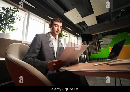 Fokussierter Mann, der in einem Bürosessel durch die Papiere schaute Stockfoto