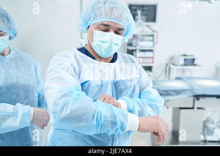 Leitender Chirurg, der Uniform für die Operation aufsetzt Stockfoto