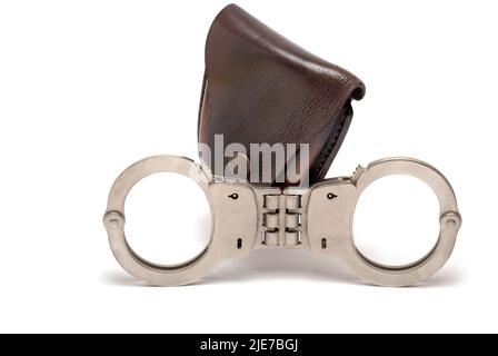 Nahaufnahme Polizei Eisen Metall Stahl Handschellen mit starren Zwischenstück vor dem dunklen Lederkoffer geschlossene Handgelenksperren auf weißem Hintergrund A Stockfoto