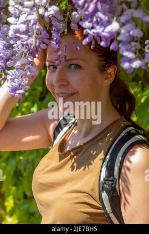 Schöne Frau mit Glyzinienblumen neben ihrem Gesicht im Sommer Stockfoto