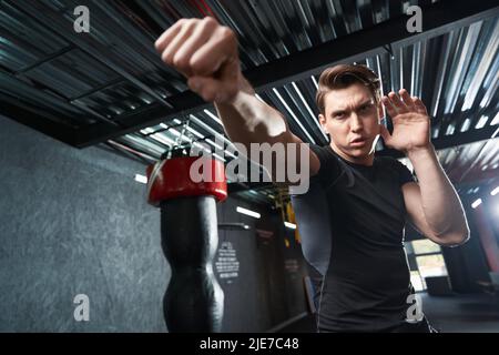 Entschlossener junger Boxer, der im Fitnessstudio Schläge übt Stockfoto
