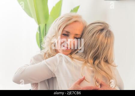 Eine unkenntliche kaukasische Frau mit glattem blondem Haar umarmt eine elegante Dame mittleren Alters mit welligen Haaren. Supportkonzept. Hochwertige Fotos Stockfoto