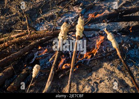 Am Lagerfeuer gekochtes Stockbrot. Brotteig auf Holzstäbchen verdreht und auf Feuer geröstet. Spaß Camping Essen für Kinder. Strand Picknick Grill oder Grill. Stockfoto