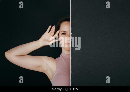 Eine schöne Brünette gucken hinter einem schwarzen Bildschirm hervor. Nahaufnahme eines jungen Mädchens, das ihre Hand an ihr Gesicht hält. Stockfoto