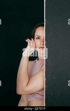 Eine schöne Brünette gucken hinter einem schwarzen Bildschirm hervor. Nahaufnahme eines jungen Mädchens, das ihre Hand an ihr Gesicht hält. Stockfoto