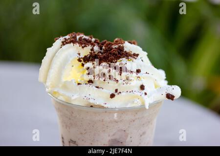 Frappekaffee mit Plätzchen-Krümel, Schlagsahne, Schokoladenbröseln in Kunststoffglas auf grünem, natürlichem Hintergrund. Eisiger Drink, erfrischend für heißen Sommertag Stockfoto