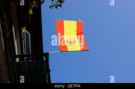 Spanische Flagge. Gelbe rote Fahne flattert im Wind gegen den blauen Himmel. Eine Flagge schmückt den Balkon des Apartmentgebäudes. Ein Symbol der Unabhängigkeit. Spanische Nation Stockfoto