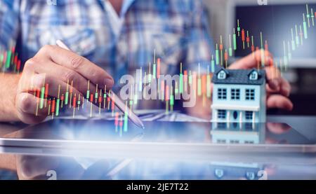Männliche Hände halten einen Stift in der Nähe der Tablette, Holzhaus auf dem Tisch. Steuerzahlungen, Investitionen und Banking-Konzept. 2023 Neujahr spart Geld und Finanzen Stockfoto