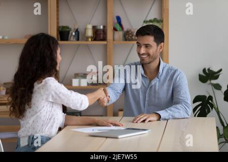 Geschäftsleute geben sich nach Verhandlungen einen Handschlag, sitzen im Büro des Unternehmens am Schreibtisch Stockfoto