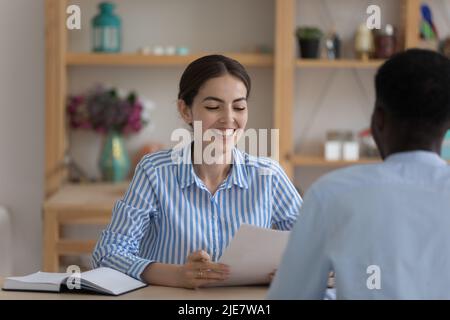 Junge attraktive Personalmanagerin, die afrikanische männliche Bewerberin interviewend Stockfoto