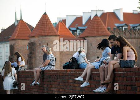 Warschau, Polen. 25.. Juni 2022. Die Menschen genießen den Sommerabend in der Warschauer Altstadt, während sie an den alten Backsteinmauern in der Nähe des Warschauer Barbicans sitzen. Tägliches Leben am Sommerabend in der Warschauer Altstadt nach einem heißen Samstag. (Foto von Volha Shukaila/SOPA Images/Sipa USA) Quelle: SIPA USA/Alamy Live News Stockfoto