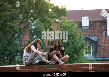 Warschau, Polen. 25.. Juni 2022. Junge Frauen entspannen sich, während sie an den alten Backsteinmauern in der Nähe des Warschauer Barbican in der Altstadt sitzen. Tägliches Leben am Sommerabend in der Warschauer Altstadt nach einem heißen Samstag. (Foto von Volha Shukaila/SOPA Images/Sipa USA) Quelle: SIPA USA/Alamy Live News Stockfoto