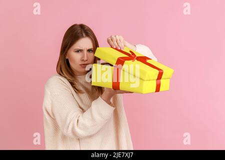 Portrait der enttäuschten jungen erwachsenen blonde Frau Eröffnung verpackt Geschenk-Box, nicht wie ihr Geschenk, Fells Trauer, trägt weißen Pullover. Innenaufnahme des Studios isoliert auf rosa Hintergrund. Stockfoto