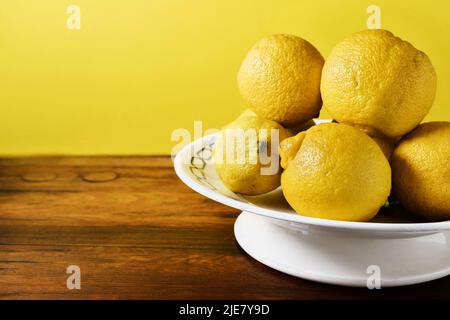 Reife Zitronen in weißem Teller auf Holztisch, gesunde Ernährung Stockfoto