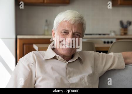 Glücklicher älterer Mann, der sich auf dem Sofa entspannt und lächelt und die Kamera anschaut Stockfoto