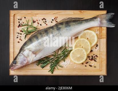 Frischer, ungekochte Zander mit Zitrone, Rosmarin und Gewürzen auf Holzbrett über schwarzem Untergrund Stockfoto