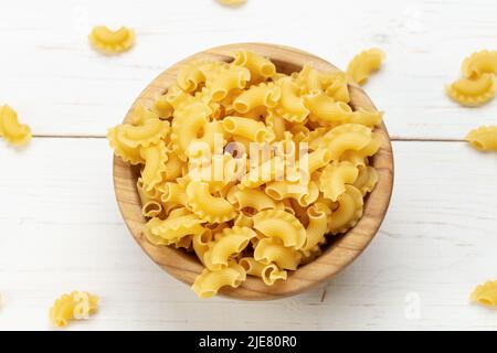 Getrocknete Makkaroni-Jakobsmuscheln. Pasta in einer Holzschüssel und auf einem weißen Tisch. Platz für Text. Stockfoto